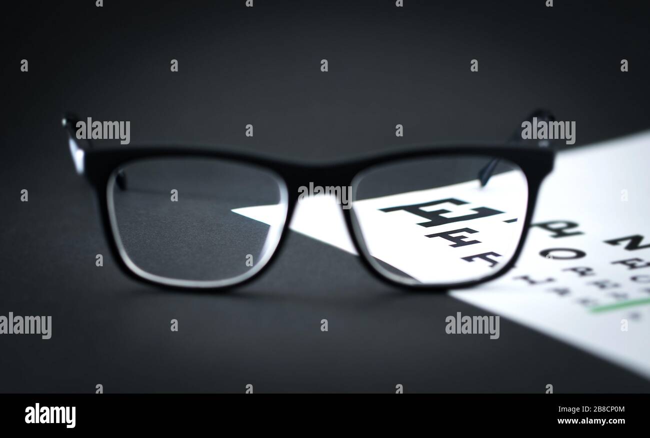 Glasses on eye test letter chart on optician table. Ophthalmology or optometry clinic. Focus through lens. Eyesight exam. Stock Photo