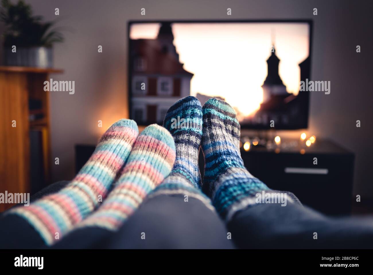 Couple with socks and woolen stockings watching movies or series on tv in winter. Woman and man sitting or lying together on sofa couch at home. Stock Photo