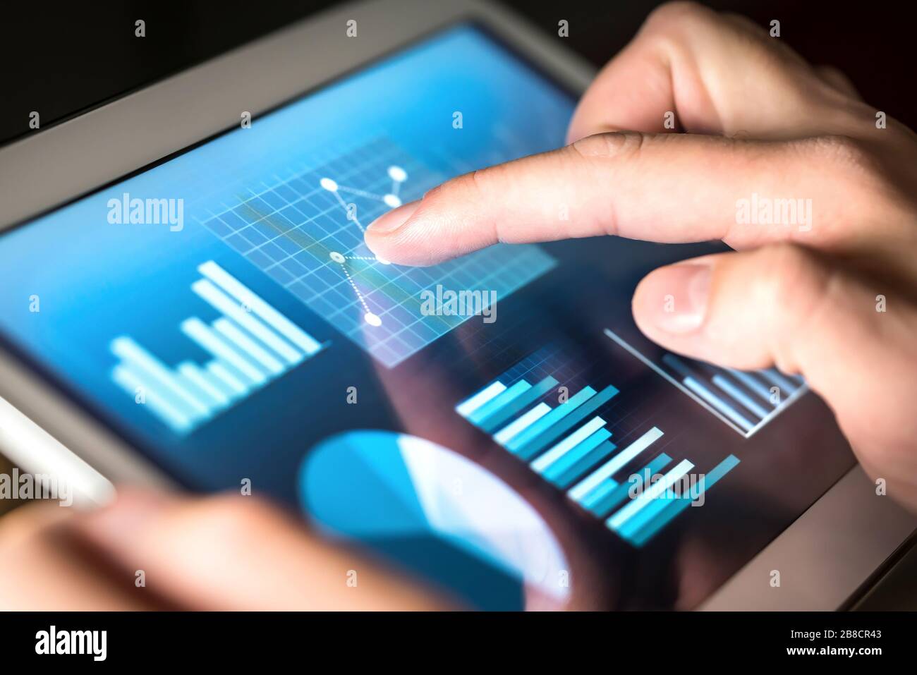 Business figures, graphs, chart and statistics. Market or economic report for financial analysis. Man working and using tablet. Finger touching screen. Stock Photo