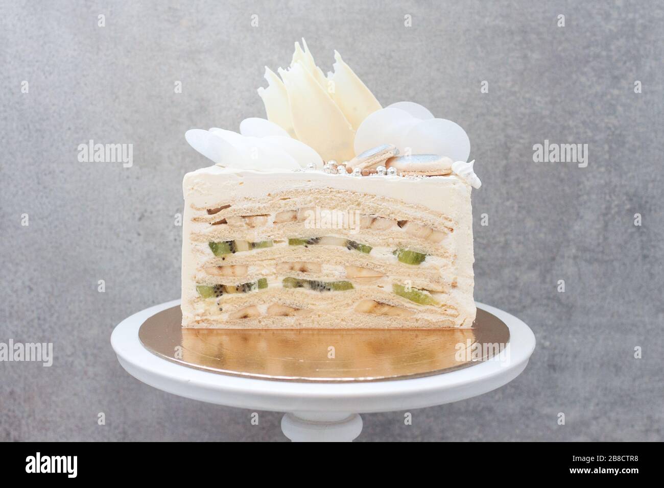 Slice of layered vanilla sponge cake with fresh bananas and kiwi inside on gray background Stock Photo