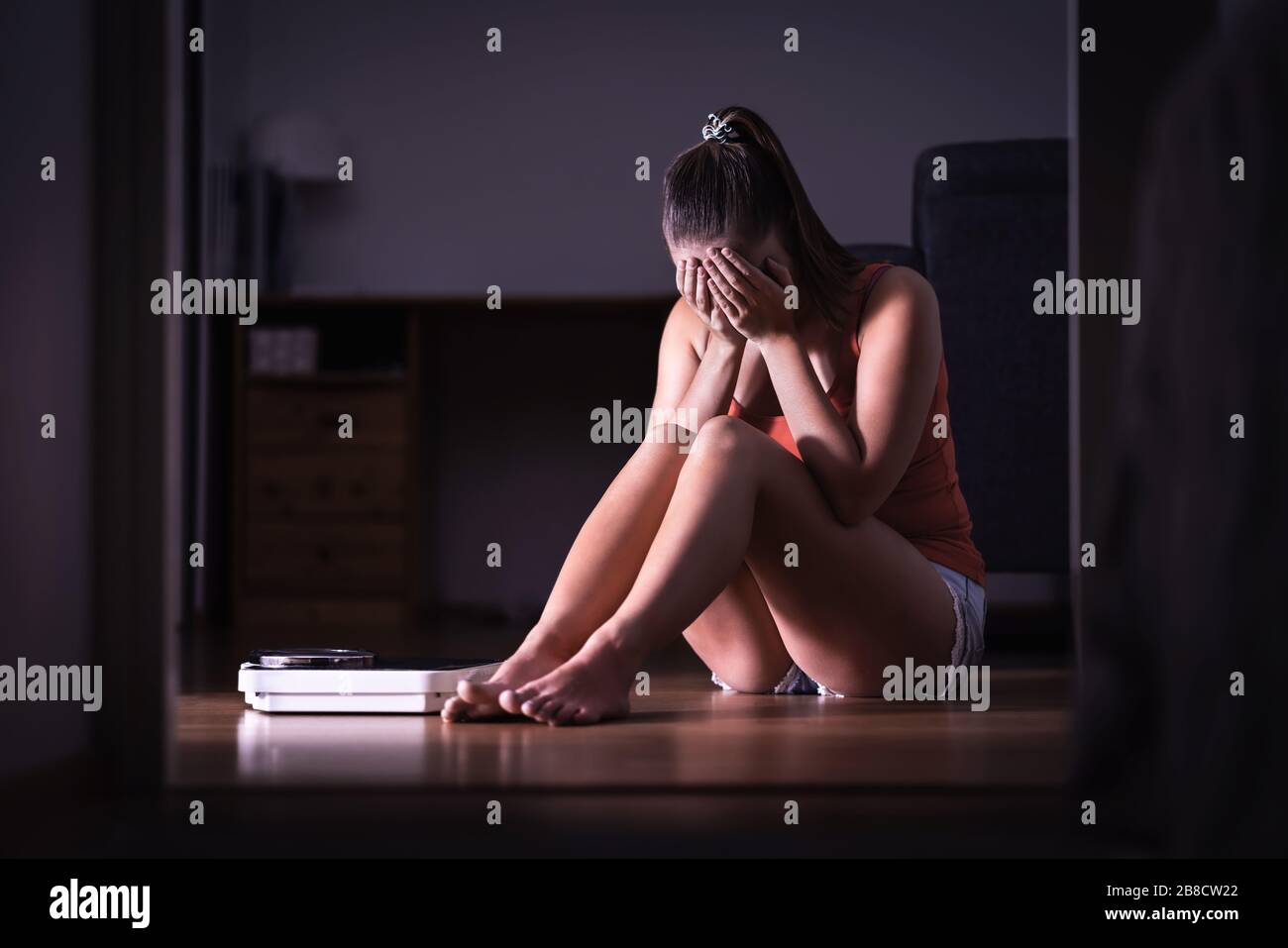 Pressure and stress about weight loss, diet or gaining weight. Eating disorder, anorexia or bulimia concept. Frustrated woman sitting on floor. Stock Photo
