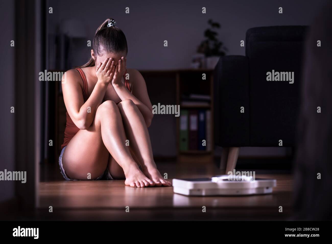 Woman having stress about weight loss, diet or gaining weight. Eating disorder, anorexia or bulimia concept. Young girl crying and sitting. Stock Photo