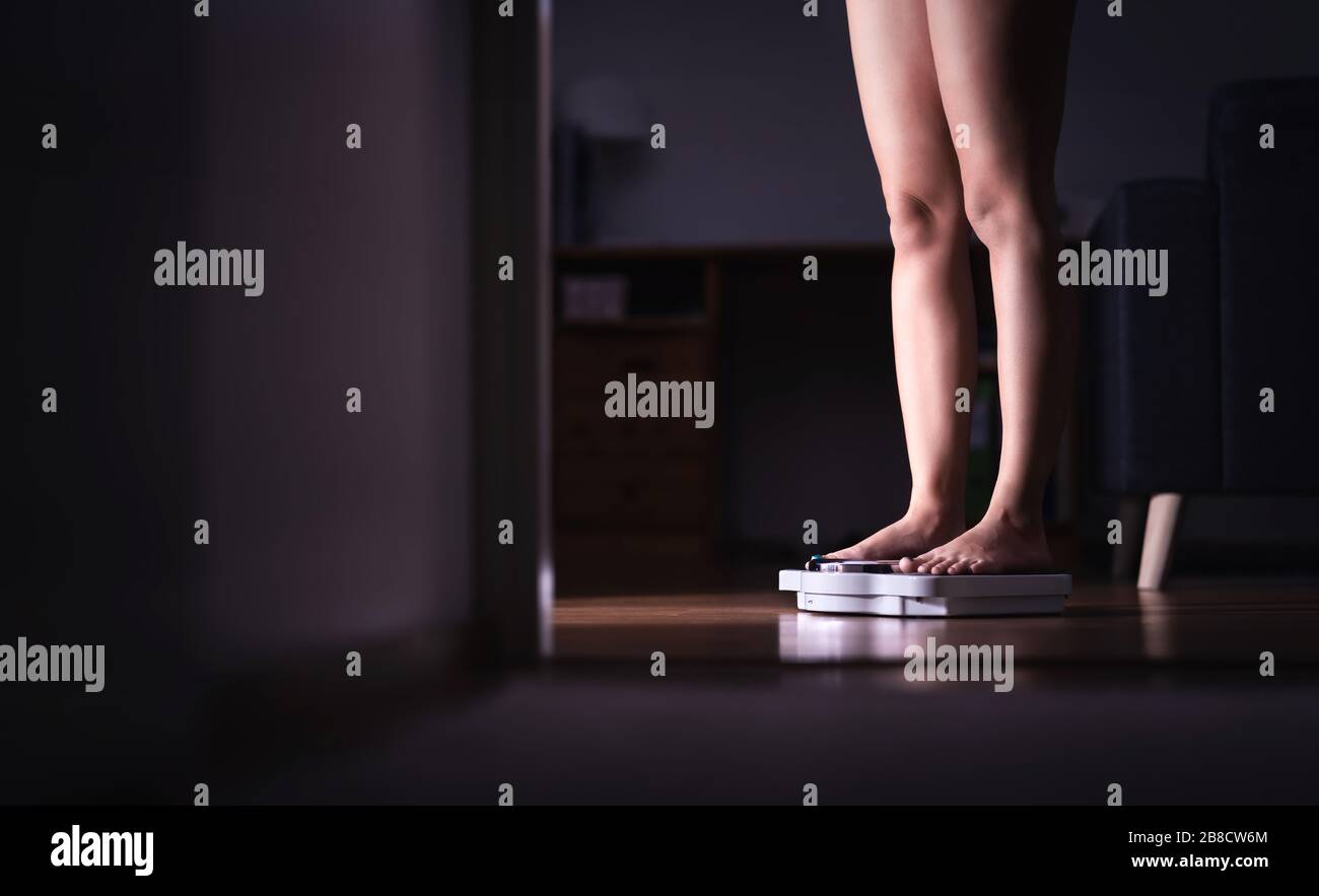 Lady standing on scale. Weight loss and diet concept. Woman weighing herself. Fitness lady dieting. Weightloss and dietetics. Dark late night mood. Stock Photo