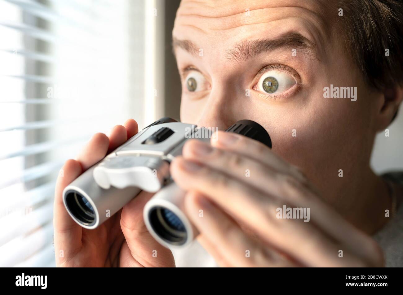 Surprised man with binoculars. Curious guy with big eyes. Nosy neighbour stalking or snooping secrets, gossip and rumour. Silly funny face. Stock Photo