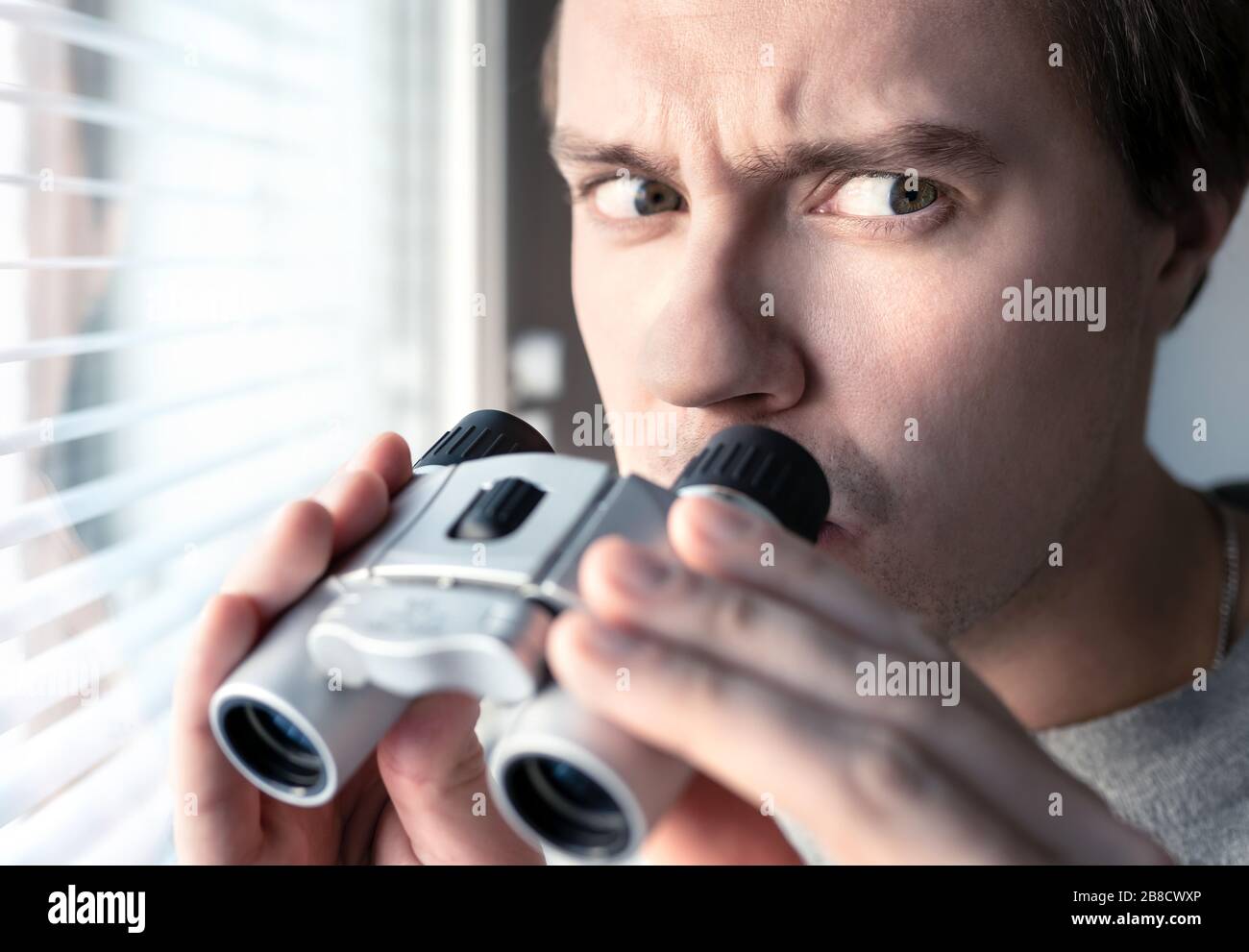 Suspicious, skeptic and confused man with binoculars. Conspiracy theory, paranoia, skepticism or suspicion concept. Curious or paranoid person looking. Stock Photo