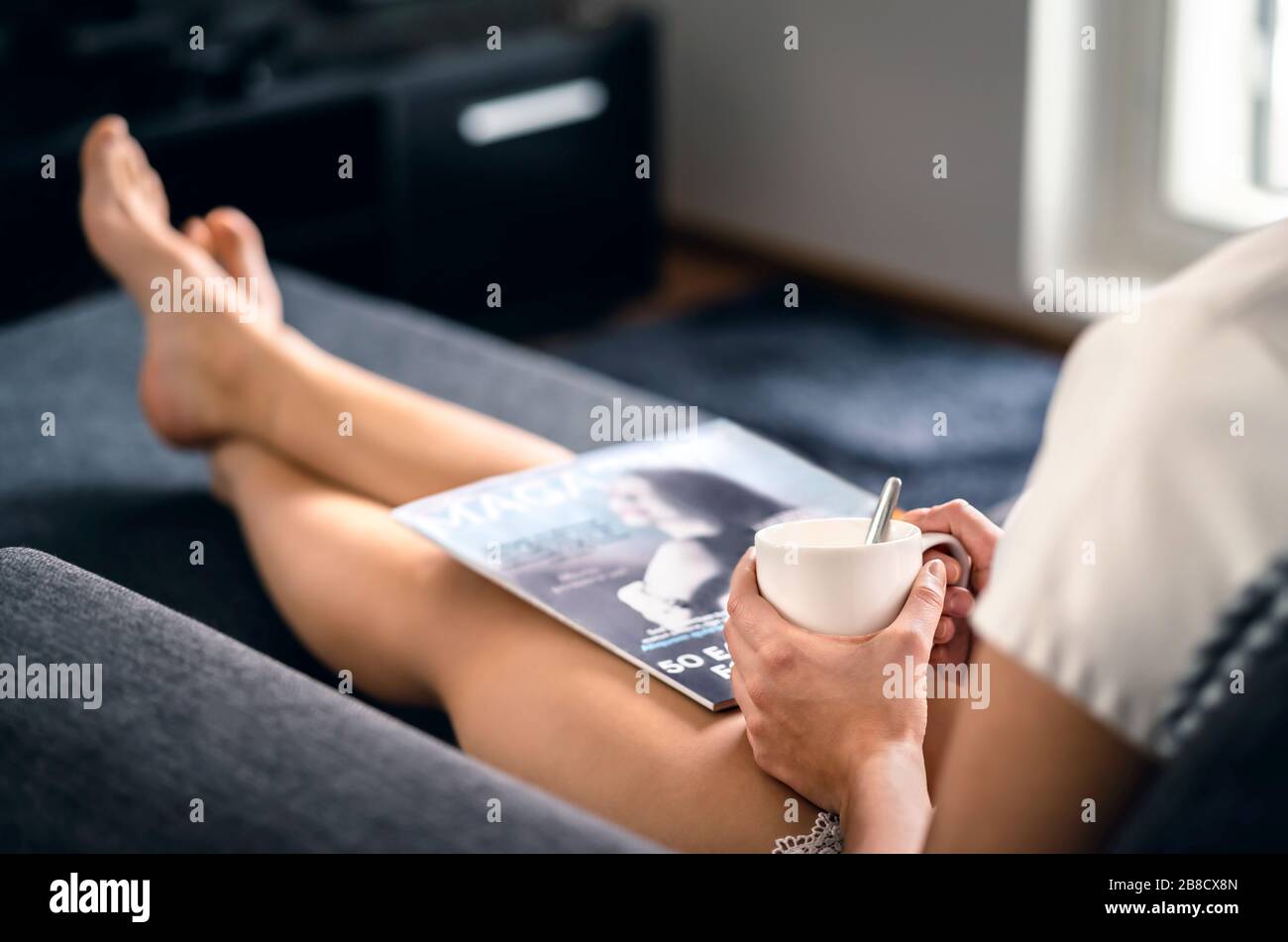 Sunday morning with magazine and coffee. Happy millennial woman relaxing with fashion and beauty trends news and cup of tea. Lady enjoying day off. Stock Photo
