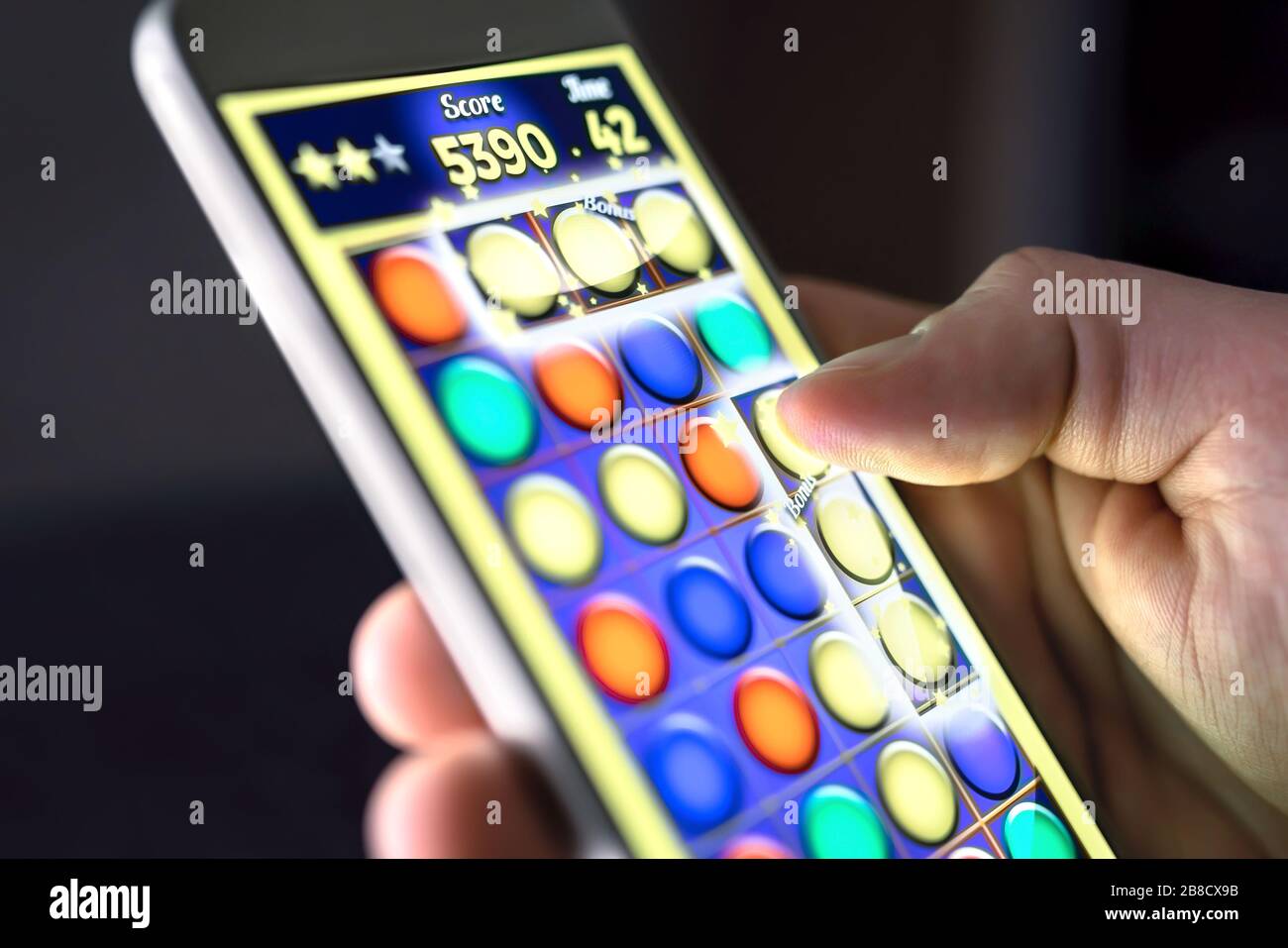 Mobile game in smartphone screen. Young man playing puzzle game in phone app. Gamer having fun. Digital gaming, entertainment and videogame concept. Stock Photo