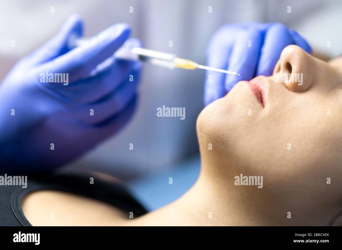 Plastic surgery, lip injection and augmentation or beauty treatment concept. Doctor with gloves and filler needle and syringe injecting lips for woman. Stock Photo