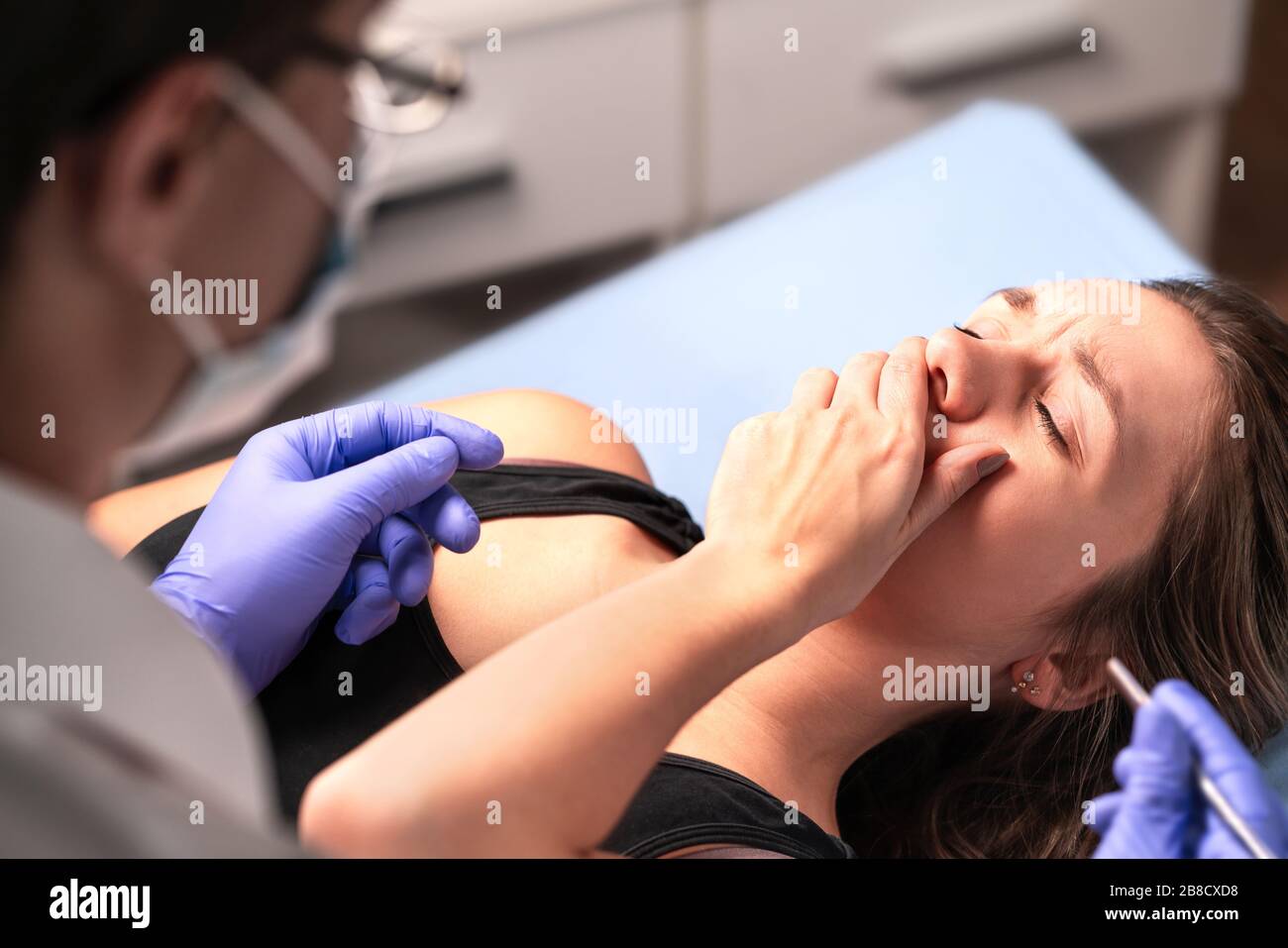 Upset patient having panic attack. Afraid of dentist or fear of doctor. Nervous woman covering mouth. Malpractice or wrong medical treatment. Stock Photo