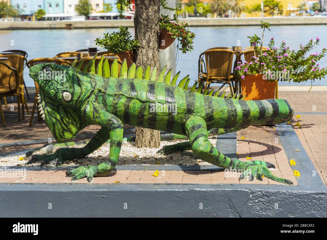 Close up view of big green iguana figure as decoration of outdoor restaurant. Saint Anna Bay and colorful buildings on background. Willemstad. Curacao Stock Photo