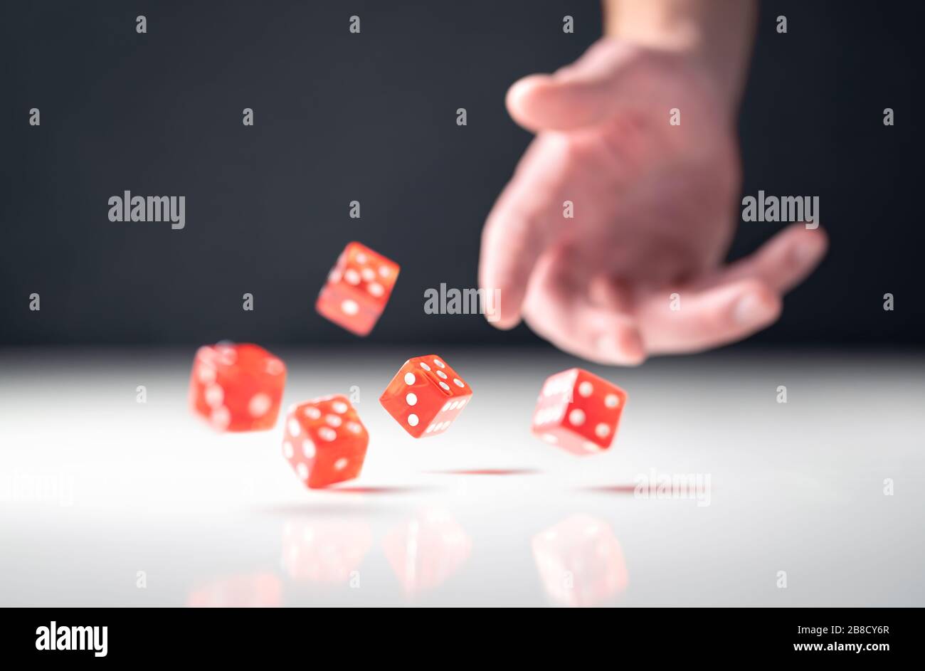 Hand throwing and rolling dice. Gambler tossing five red poker and casino dice on table. Man gambling or playing board game. Risk, luck, betting. Stock Photo