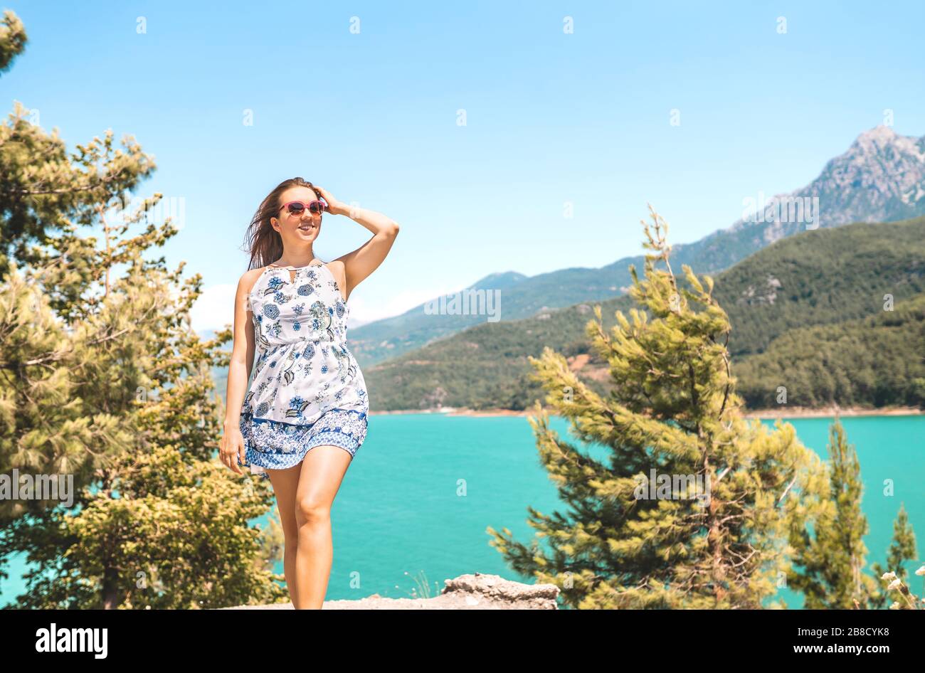 Woman walking in nature, mountain in the background. Adventure, freedom and carefree lifestyle. Millennial lady in summer dress. Landscape with valley. Stock Photo