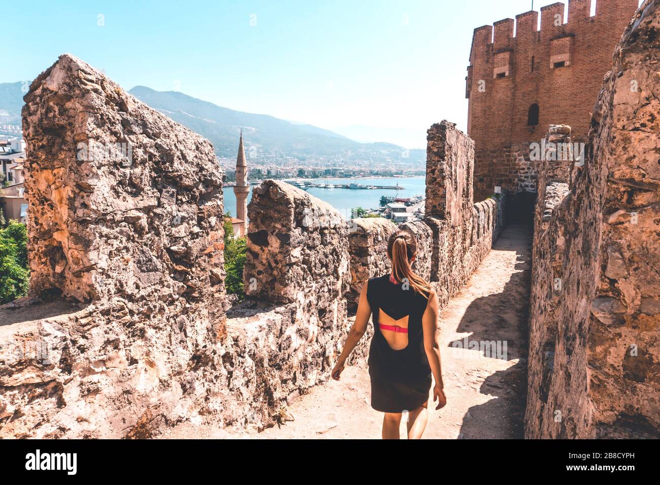 Traveler exploring the city of Alanya in Turkey. Woman walking and discovering old landmark in Europe. Tourist sightseeing in the Red Tower. Stock Photo