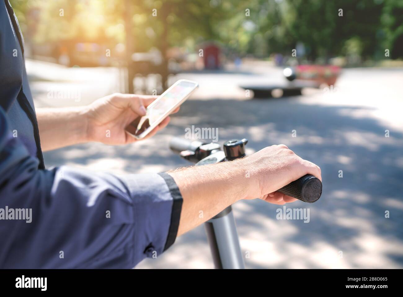 Electric scooter in city. Man using smartphone to rent an e kick vehicle. Millennial guy with mobile phone using eco transport in downtown. Stock Photo