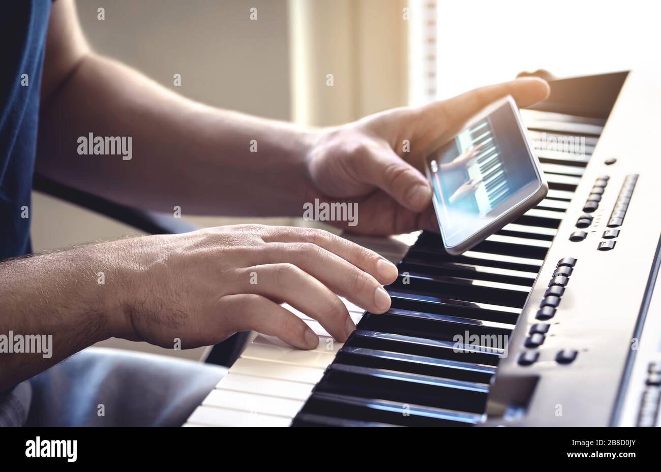 Man watching piano tutorial video with mobile phone. Person practising playing with an online lesson and course. Internet class to learn. Stock Photo