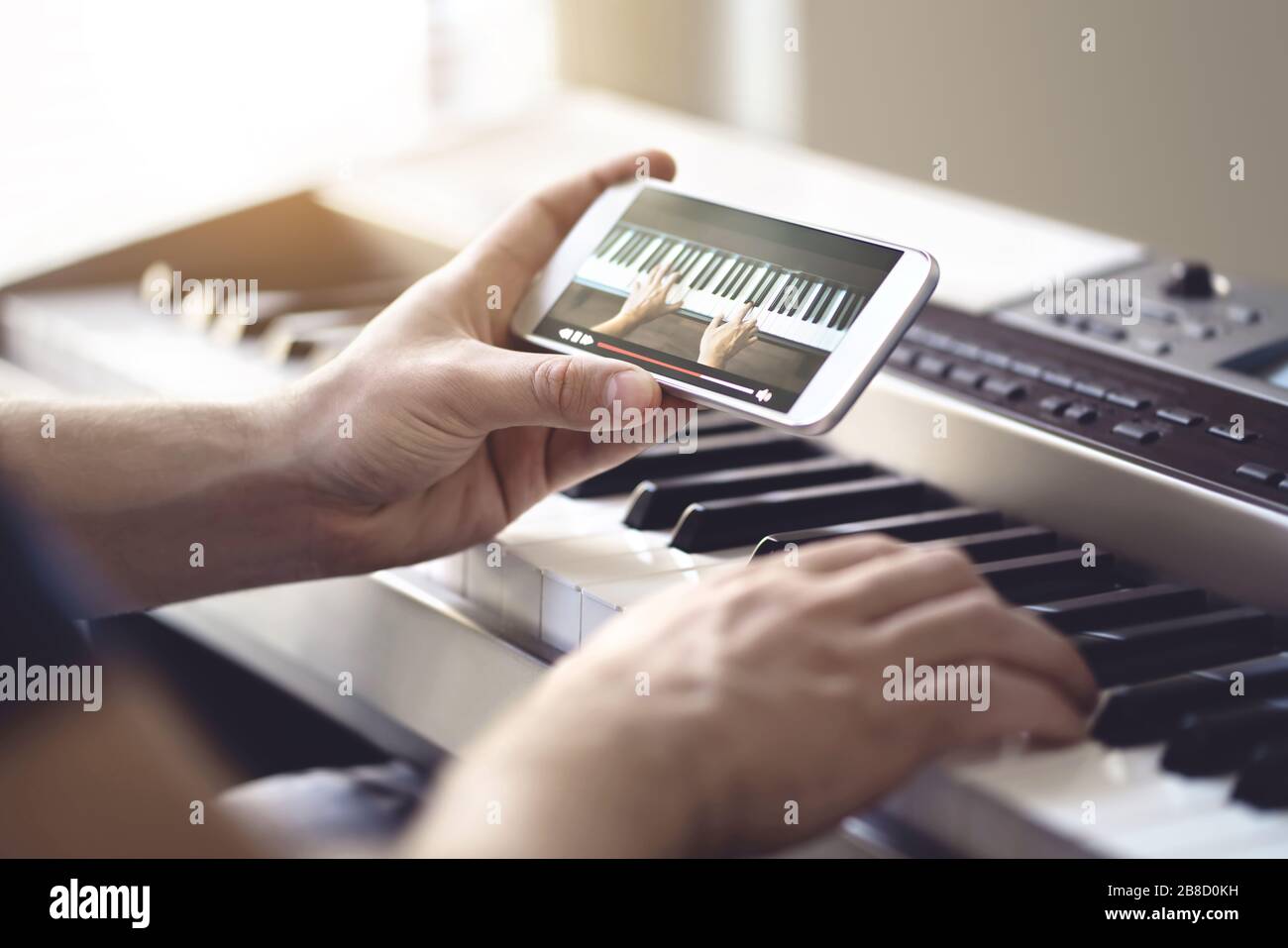 Piano lesson online. Man watching video tutorial with mobile phone and practising playing. Person learning to play an instrument. Stock Photo