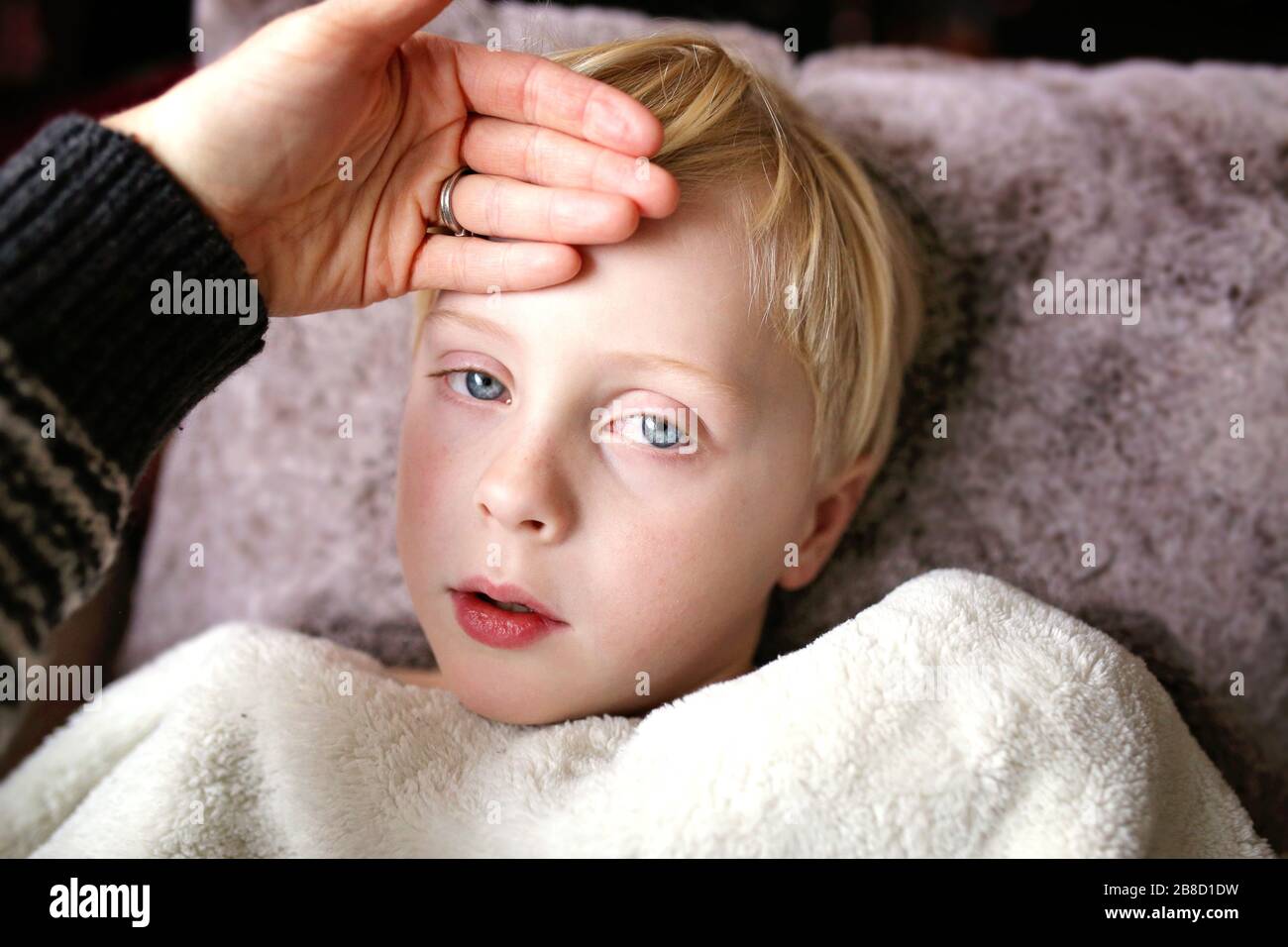 A mother's hand is feeling the temperatur of a young child with a fever who is sick with influenza. Stock Photo