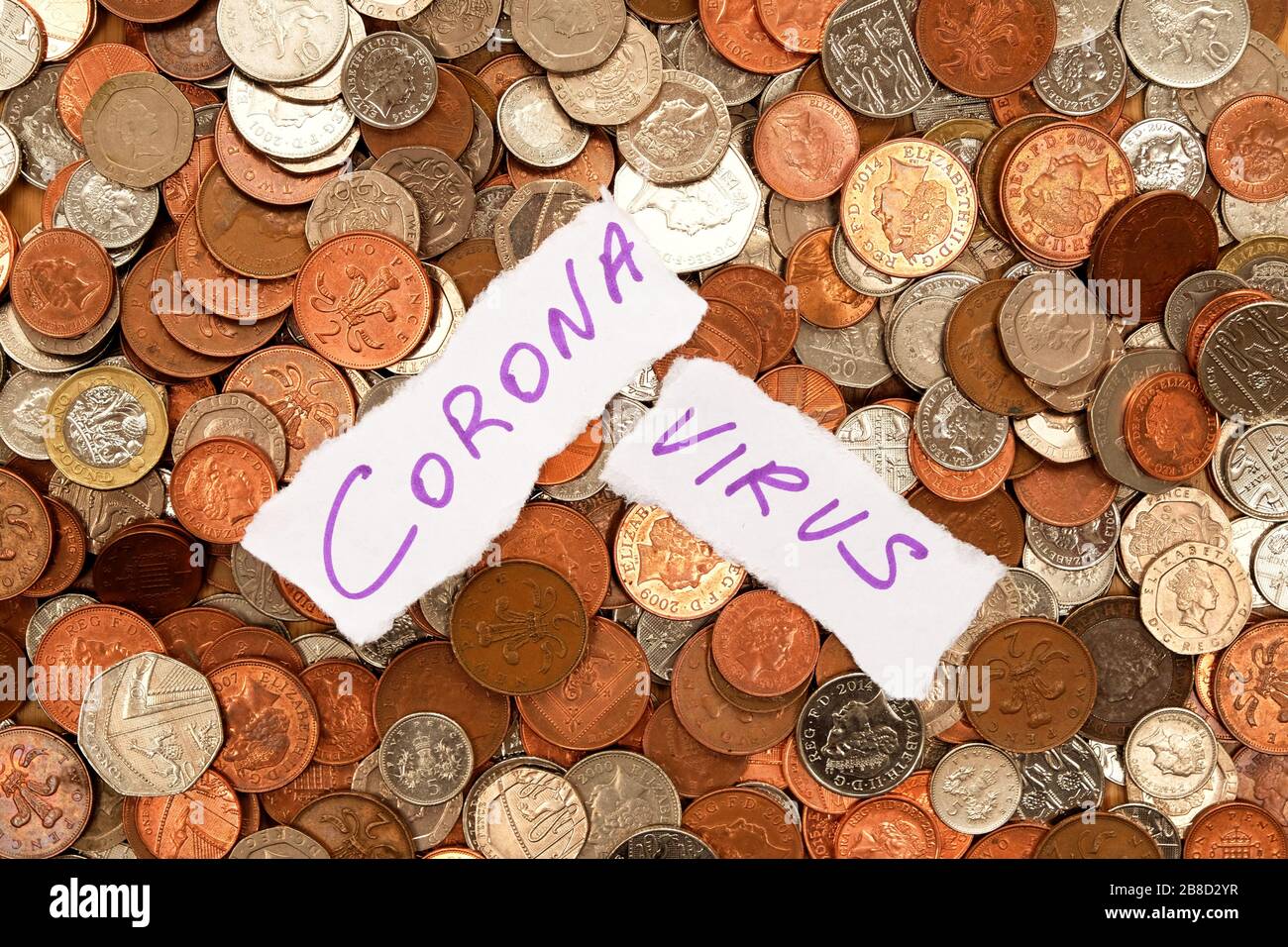 The words corona virus written in purple ink on two pieces of ripped white paper the paper is laying on top of hundreds of silver and copper coloured Stock Photo
