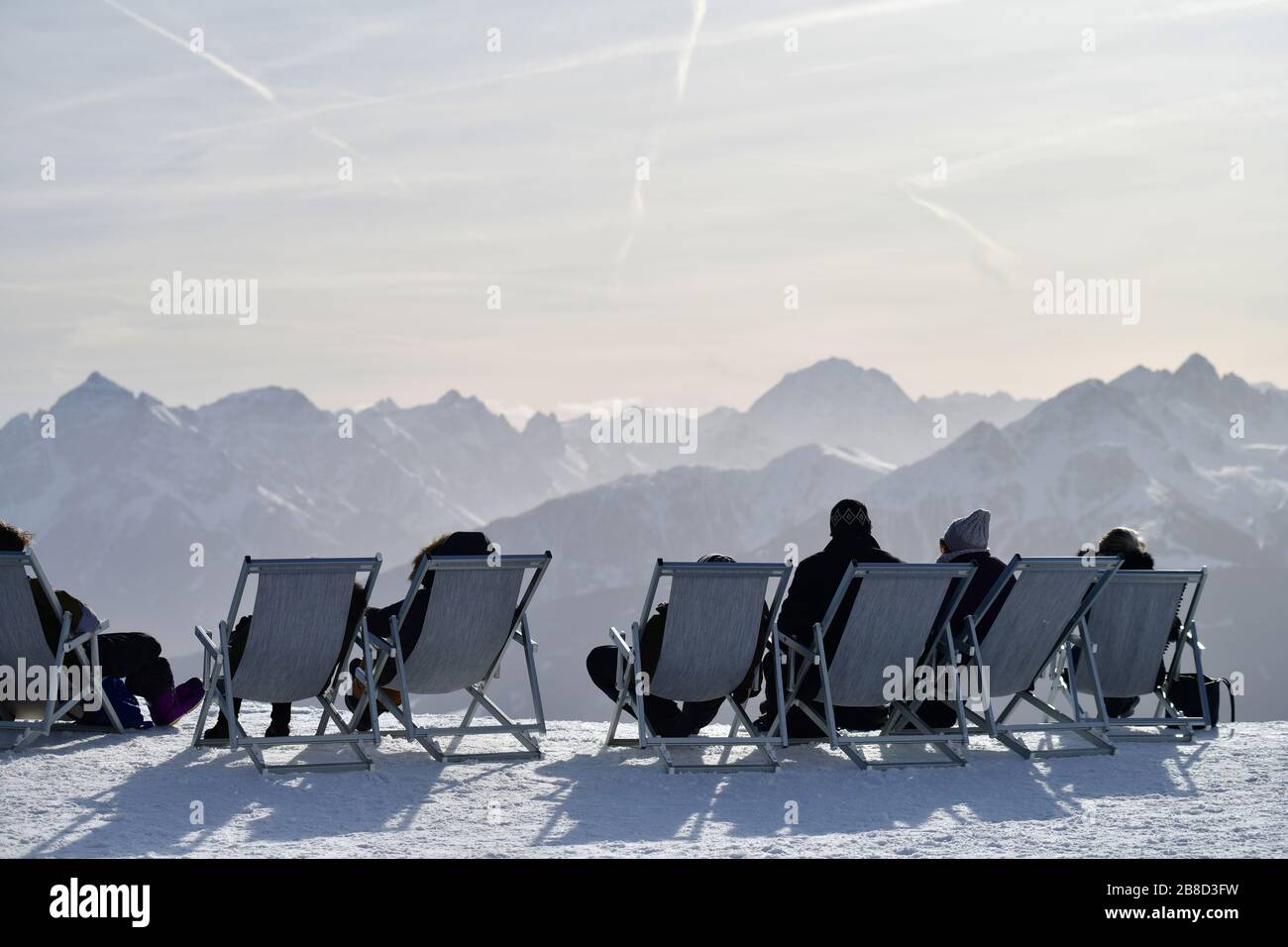 A row of sun loungers with sunbathers taking a ski break high on the summit of a mountain in Innsbruck during winter holiday Stock Photo