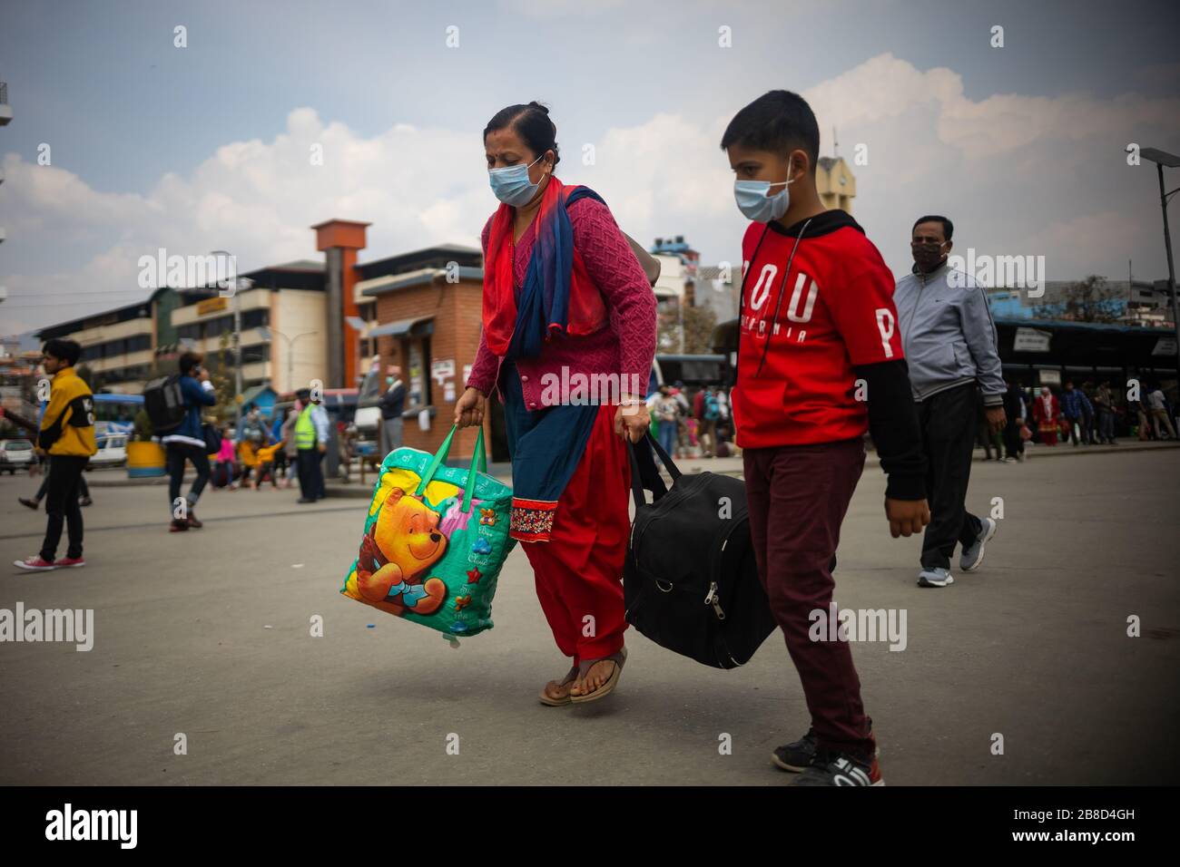 Mother and son carrying their belongings towards the bus park during the corona virus pandemic.Kathmandu's new bus park is crowded after government decides to halt long-tour vehicles amidst Covid-19 fears, effective from March 23 to March 31. The last three days saw over 500,000 leaving the capital. Stock Photo