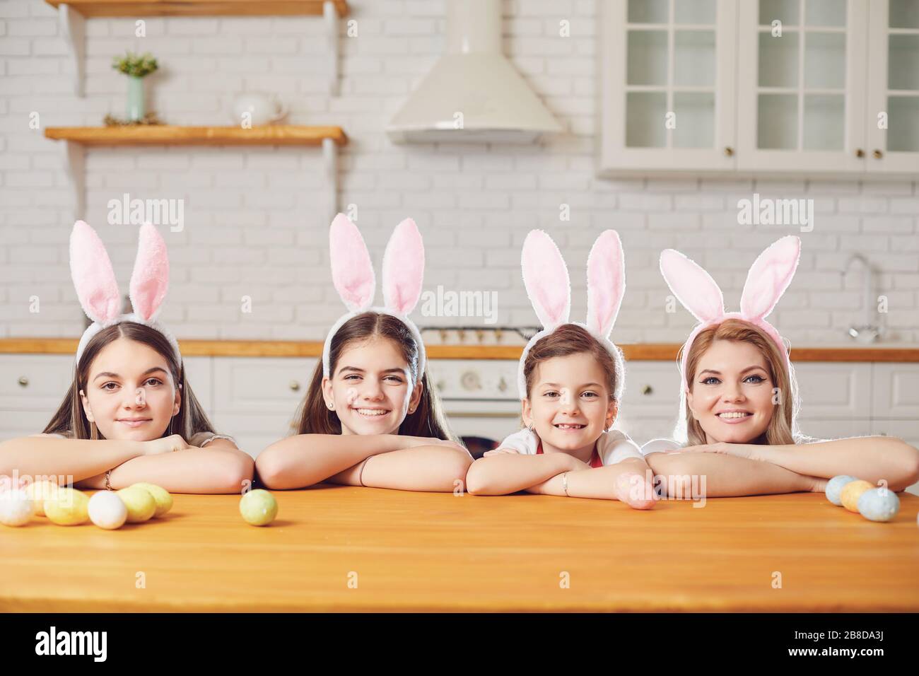 Happy easter. Mother and daughters with rabbit ears decorate Easter eggs at a table in kitchen. Stock Photo