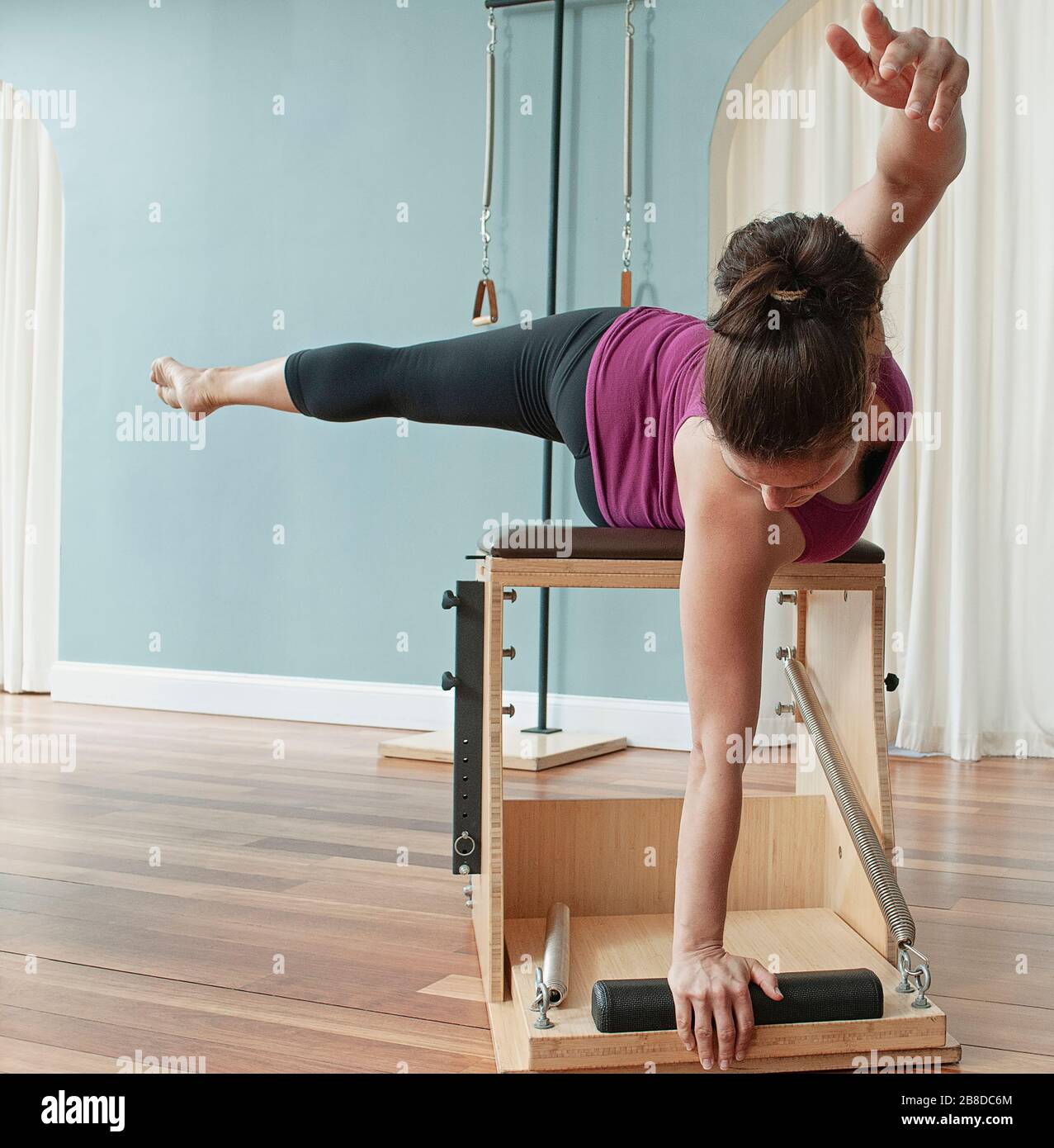 A woman doing a Pilates side body twist on a chair apparatus. Stock Photo