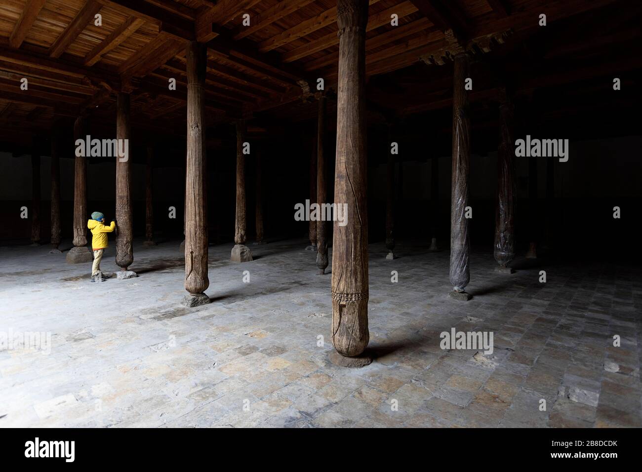 Uzbekistan, Khiva, boy in yellow jacket looking at the carved detail of the wood columns inside the old Juma mosque Stock Photo