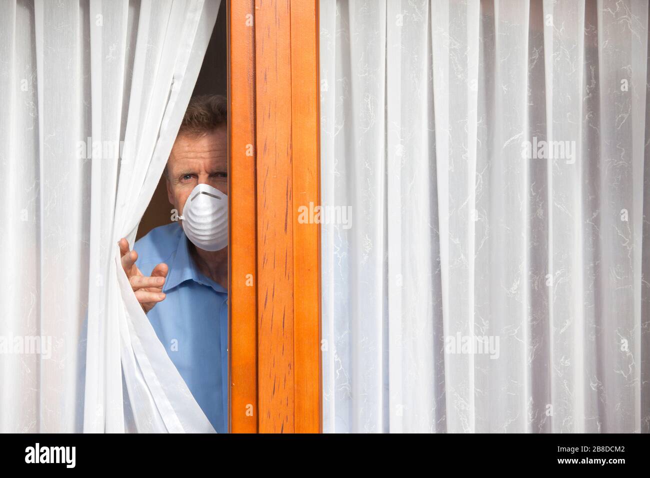 Mature man put under quarantine at home or at a hospital because of an infection or coronavirus looking sorrowful out of  a window Stock Photo