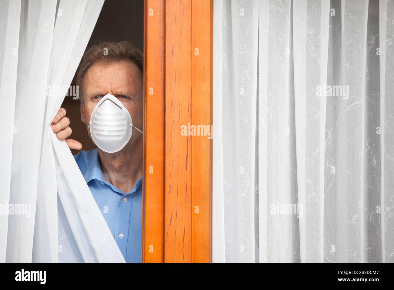 Mature man put under quarantine at home or at a hospital because of an infection or coronavirus looking seriously out of  a window Stock Photo