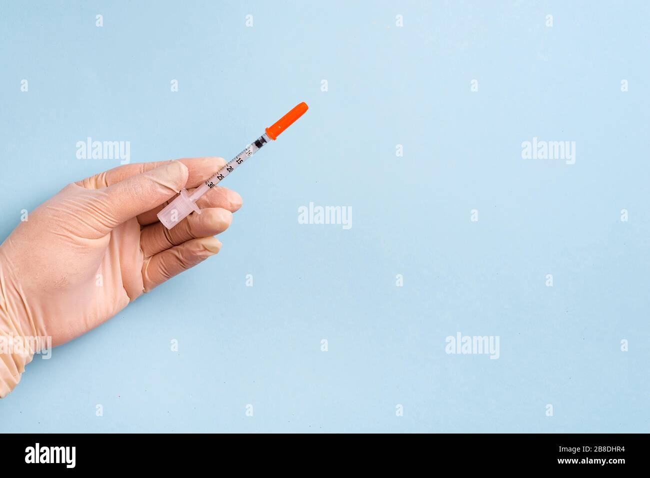 Female's hand in the medical gloves holds syringe on a light blue ...
