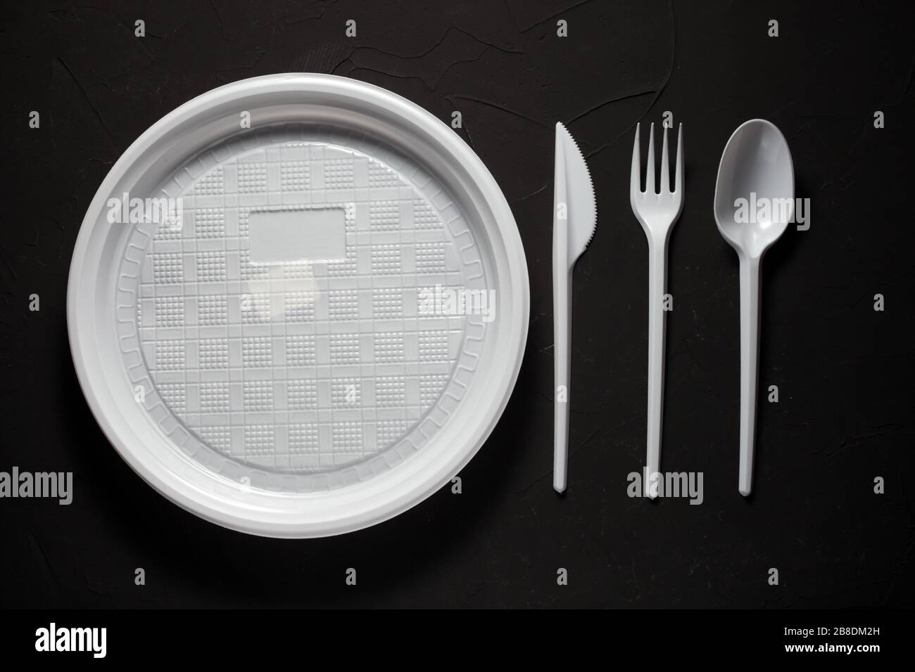 disposable plate with disposable fork, spoon, knife on a dark background Stock Photo