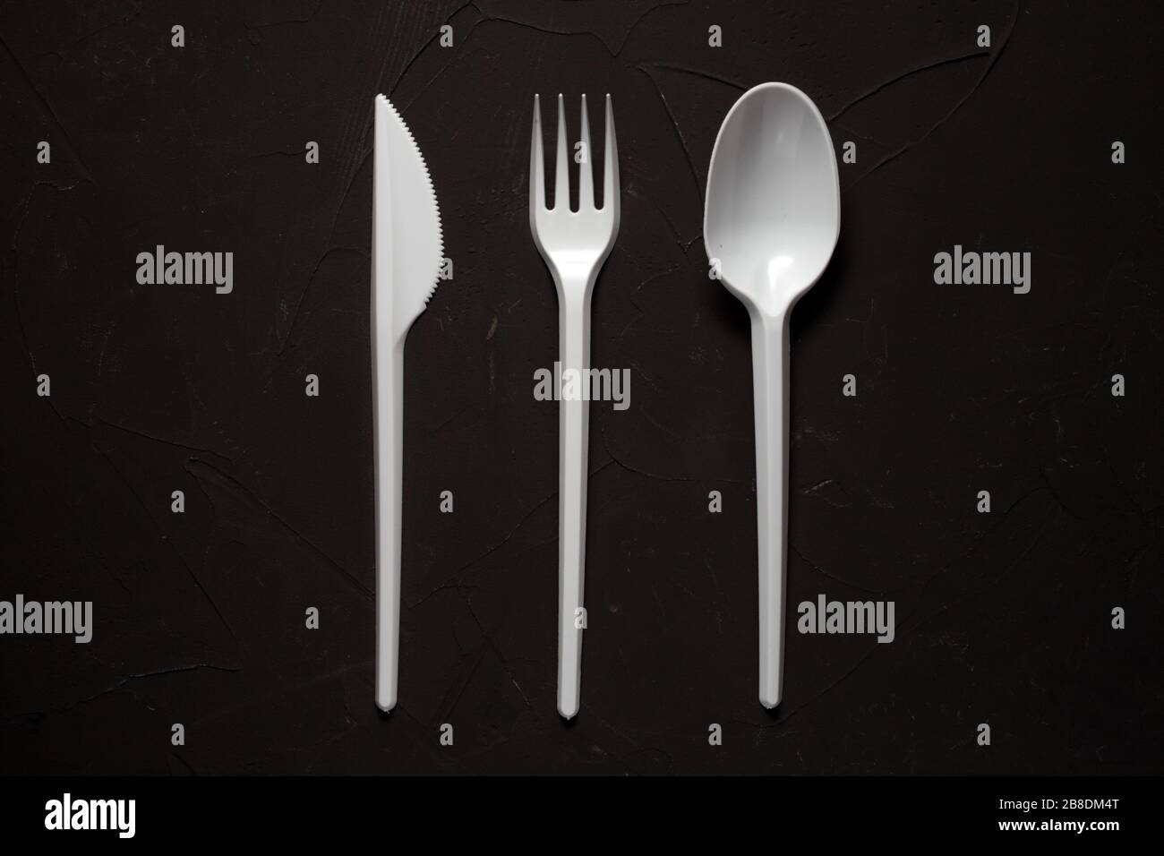 disposable fork, spoon, knife on a dark concrete background Stock Photo