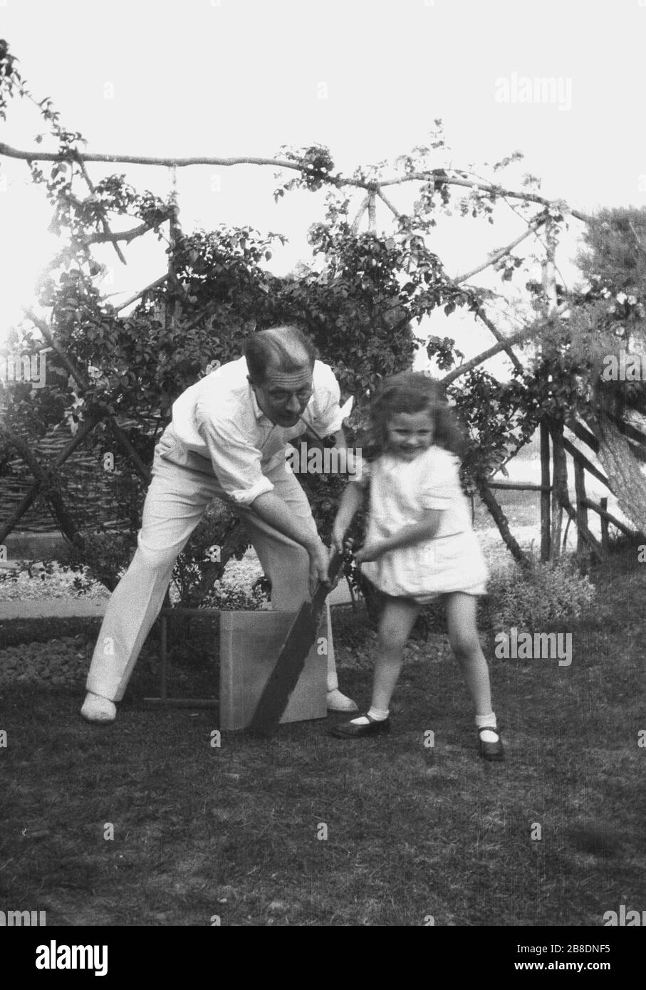 1930s, historical, dad in his cricketing whites and with a pipe in his mouth outside on some grass showing his young daughter how to use a cricket bat infront of a stool for stumps, England, UK. Stock Photo