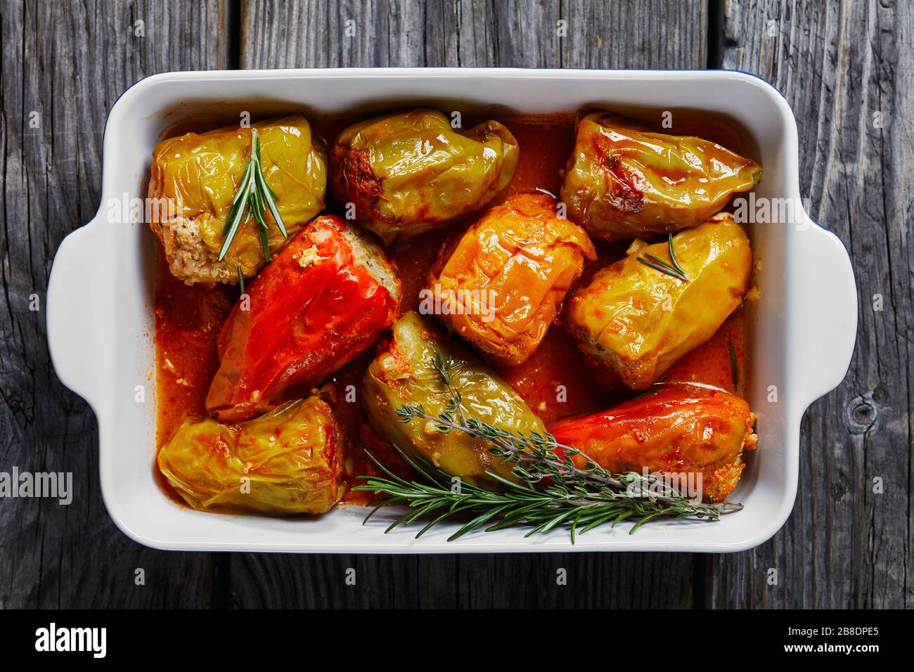 Stuffed bell peppers with rice and minced meat: beef and pork with tomato sauce, rosemary and thyme on top baked on a baking dish, on a wooden backgro Stock Photo