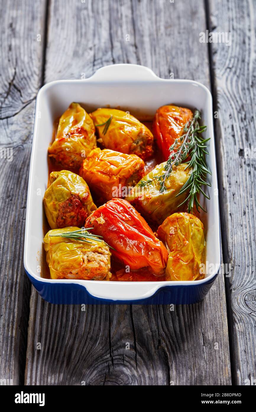 Mediterranean dish: peppers stuffed with rice and minced meat: beef and pork with tomato sauce, rosemary, and thyme on a baking dish, on a wooden back Stock Photo
