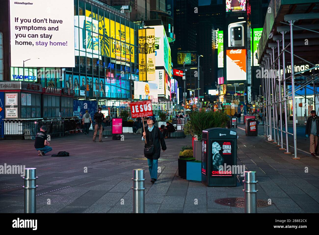 A woman holding a Jesus sign walking through a deserted Times Square at rush hour during the Coronavirus pandemic in New York City. Stock Photo