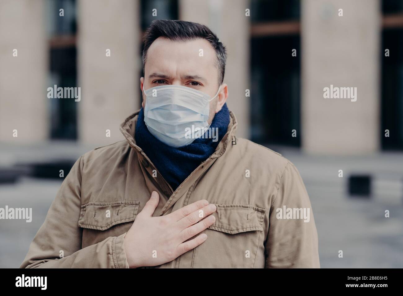 Sick man protects from coronavirus by wearing mask, keeps hand on chest