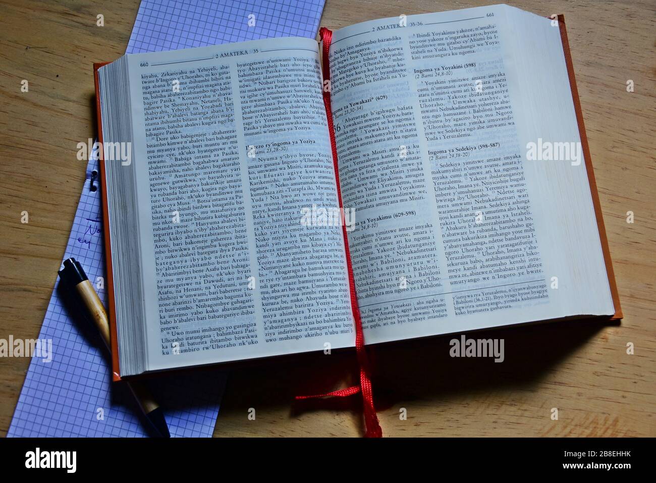 Open Kinyarwanda Catholic Holy Bible with a notebook and pen on a wooden table Stock Photo