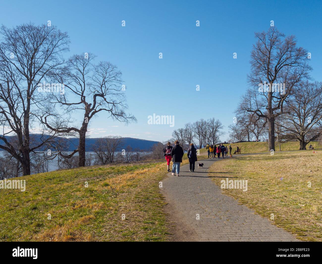 Tarrytown, NY - 21 March 2020: On the first day of spring, New Yorkers hike in Rockefeller State Park as cases of coronavirus top 10,300 in the state. Although NY Governor Andrew Cuomo has ordered all but workers in essential services such as healthcare and groceries to work from home, and to stay home except when necessary, he has also encouraged people to exercise outdoors, noting this means hiking, running, not playing basketball with groups of people. With fewer vehicles on the road, the sky, and therefore the Hudson River, are a beautiful blue. Stock Photo