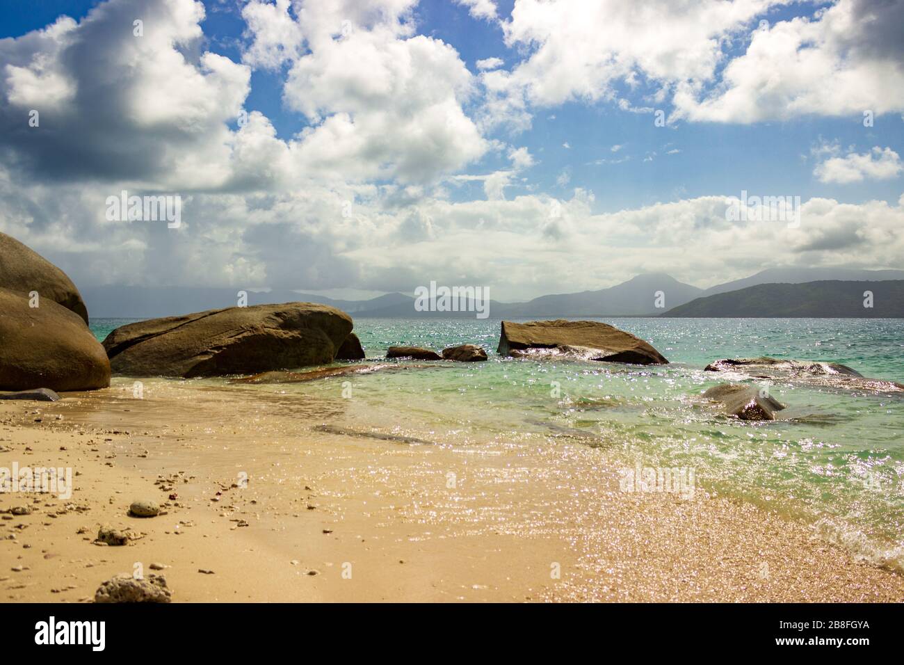 Nudey Beach, Fitzroy Island, rocks break through the crystal clear waters of the Coral Sea with the coast of Queensland Australia in the background. Stock Photo