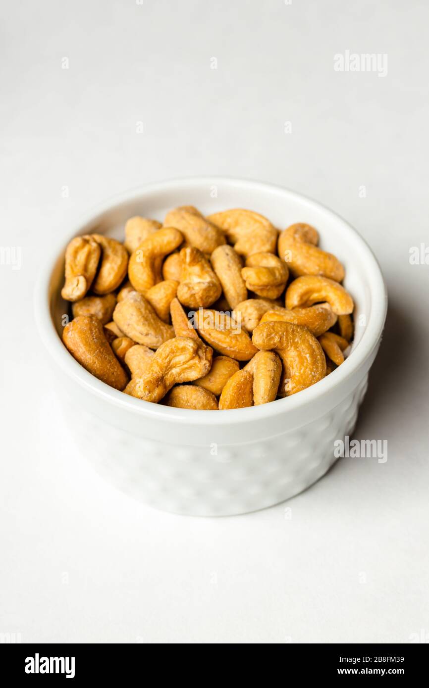 A small white bowl of delicious healthy salted cashew nuts isolated on a white background close up Stock Photo