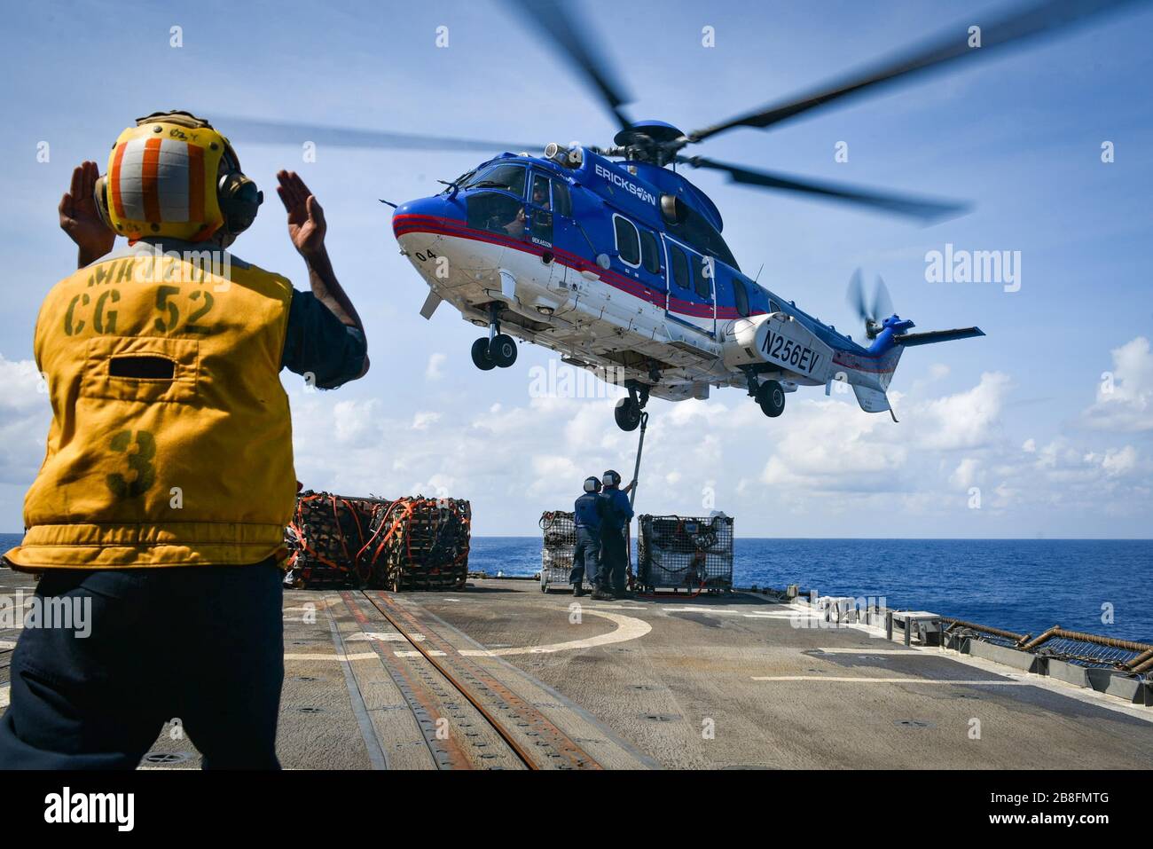 SOUTH CHINA SEA (March 14, 2020) U.S. Navy Boatswain’s Mate 2nd Class Joel Lazo, from San Jose, Calif., left, signals the pilot of a Eurocopter AS332 Superpuma, assigned to the dry cargo and ammunition ship USNS Carl Brashear (T-AKE 7),  while U.S. Navy Seaman Oluwatobiloba Kosoko, from Lagos, Nigeria, and U.S. Navy Seaman Noah Rodenburg, from St. Louis, attach a cargo leg during a vertical replenishment-at-sea aboard the Ticonderoga-class guided-missile cruiser USS Bunker Hill (CG 52) March 14, 2020. Bunker Hill, part of the Theodore Roosevelt Carrier Strike Group, is on a scheduled deploymen Stock Photo