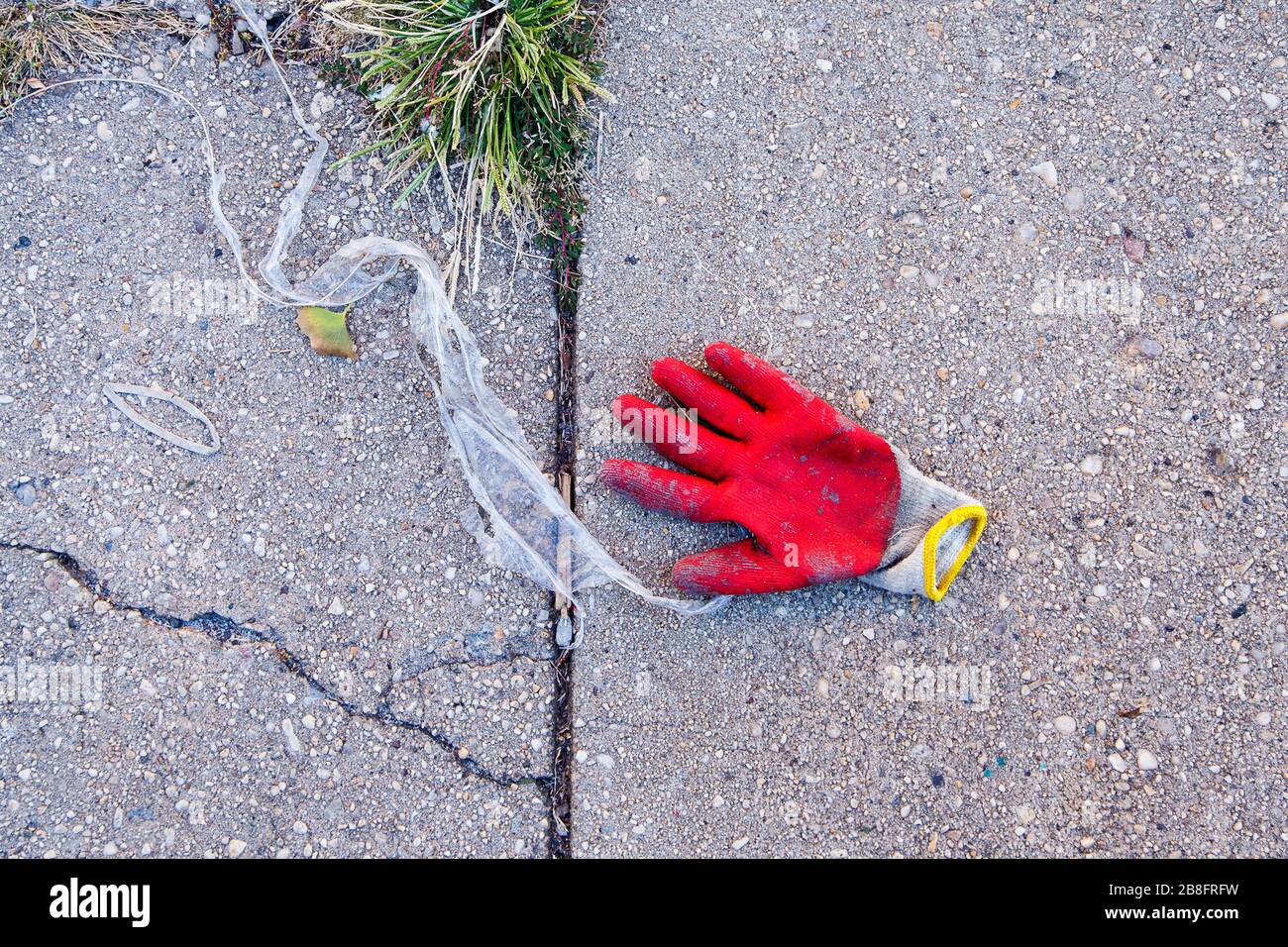 Lone red work glove on sidewalk with debris and weeds Stock Photo