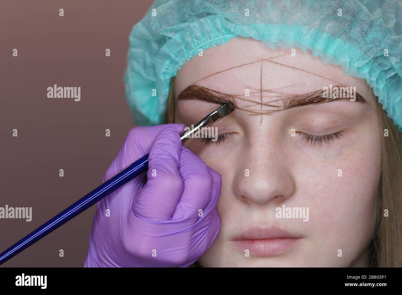 Young woman undergoing eyebrow correction procedure in beauty salon, close up. Beauty treatment at spa salon. Beautician paints eyebrows. . Stock Photo