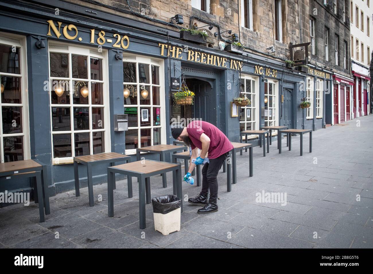 A member of staff at The Beehive Inn in the Grassmarket, Edinburgh, cleans the tables following the pub's closure due to the coronavirus outbreak. Stock Photo