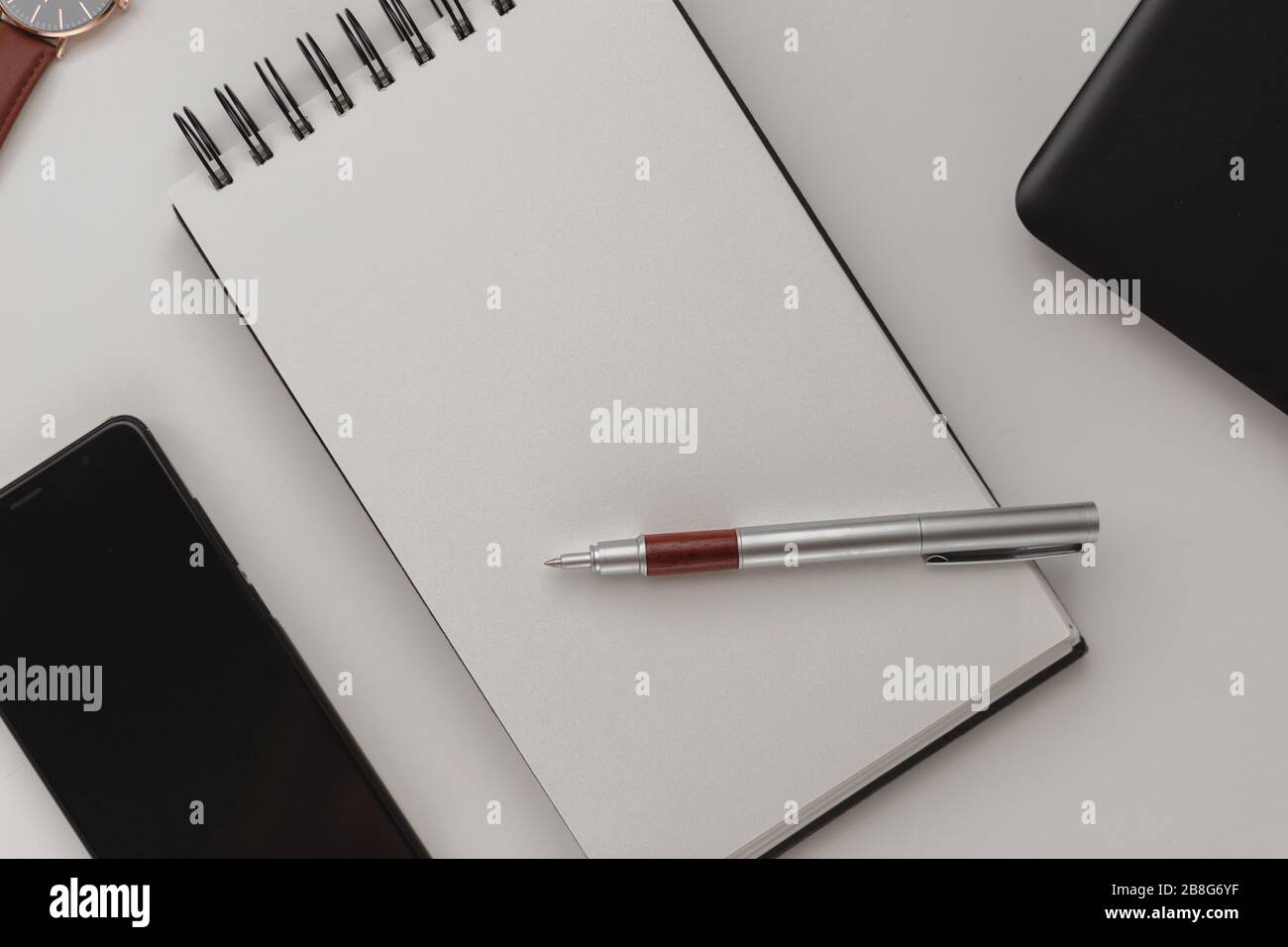 Minimalist detailed workspace background, an open spiral notebook with a blank sheet, a pen and a mobile phone. Copy space top view, flat lay, mockup. Stock Photo