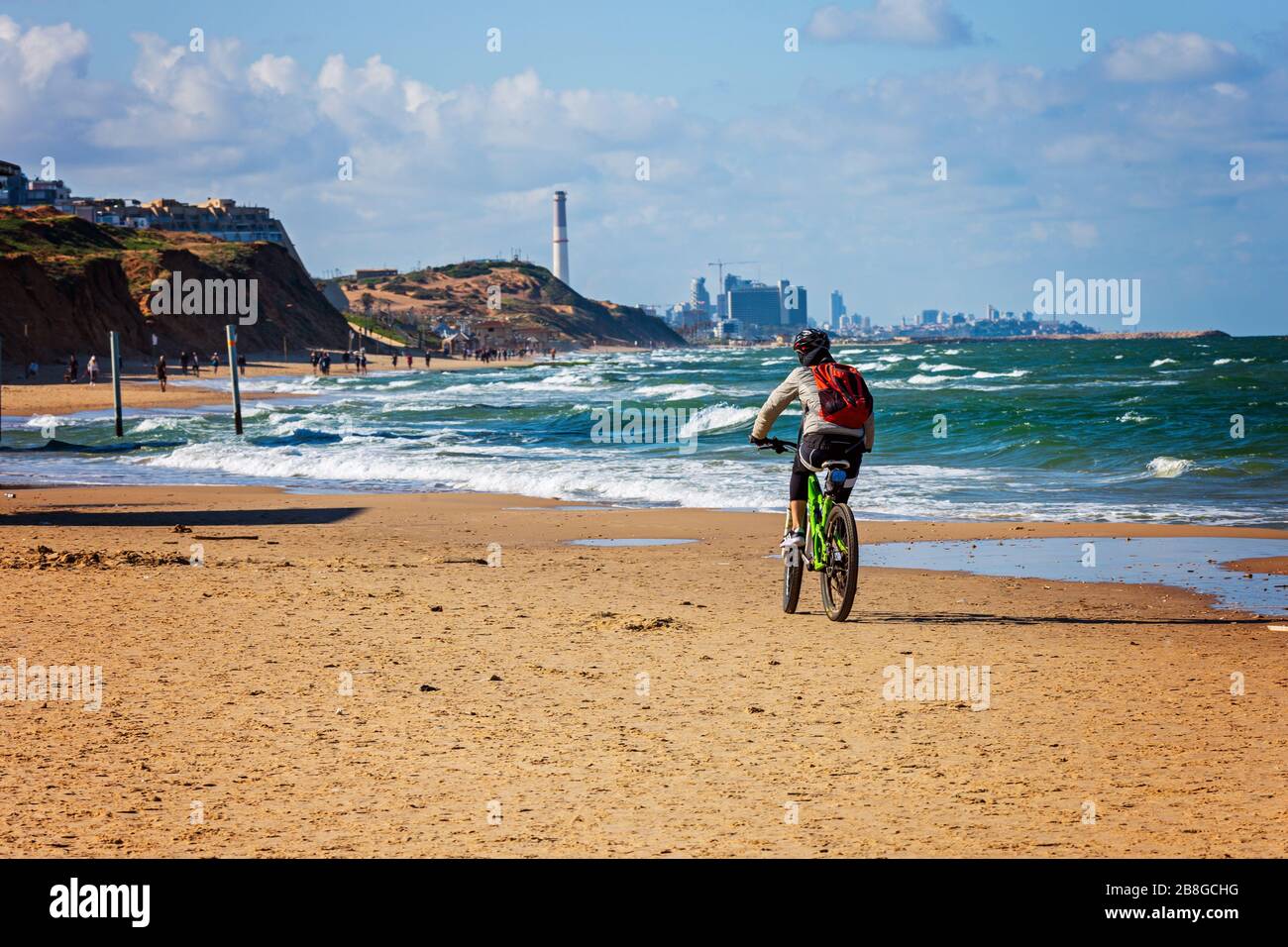 Cyclist with backpack on the carrier ridig along the sandy coast of the Gulf of Tel-Aviv Stock Photo