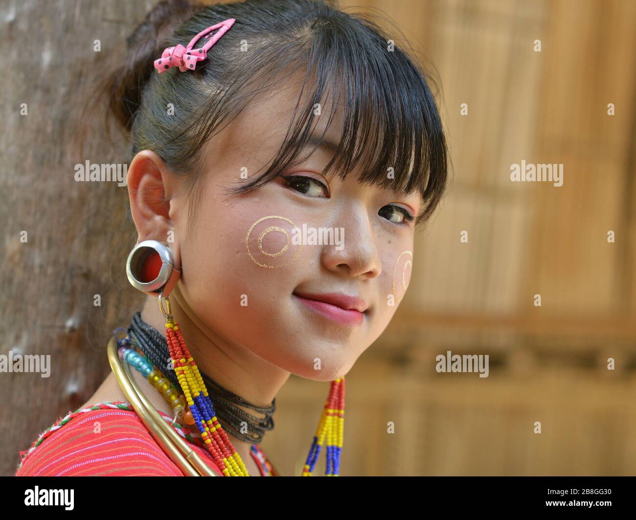 Pretty Karen Kayaw (Kayor) teenage girl with traditional thanaka face cosmetic on her cheeks and distinctive tribal earplugs smiles for the camera. Stock Photo
