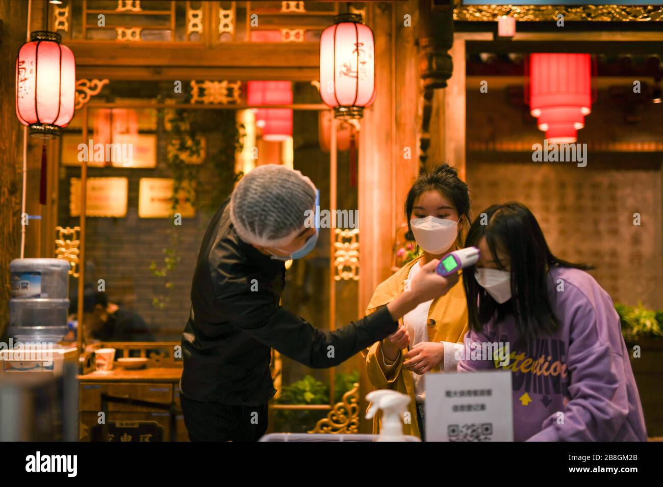 Chengdu, China's Sichuan Province. 21st Mar, 2020. A customer registers as a staff member checks her body temperature at the entrance of a restaurant in Chengdu, southwest China's Sichuan Province, March 21, 2020. The hotpot restaurants in Chengdu have resumed business gradually with measures taken to prevent the outbreak of the novel coronavirus disease (COVID-19). Credit: Tang Wenhao/Xinhua/Alamy Live News Stock Photo