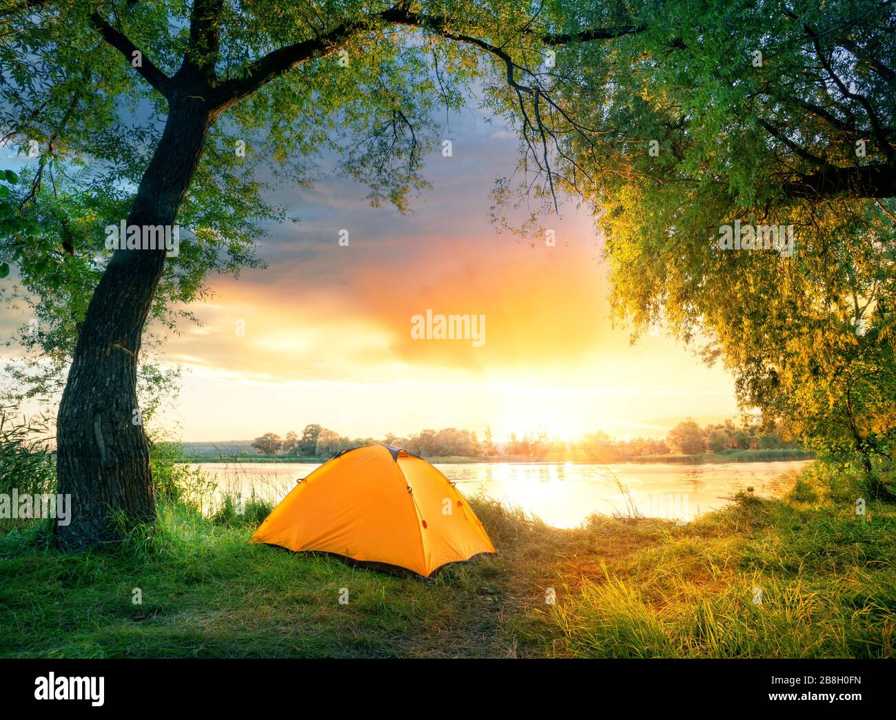 Orange tent surrounded by green leaves by river Stock Photo
